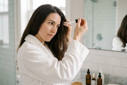 Femme appliquant un sérum anti-chute sur le cuir chevelu dans une salle de bain moderne avec des flacons de soins capillaires sur le comptoir