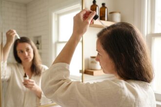 Femme appliquant un sérum capillaire sur son cuir chevelu devant un miroir de salle de bain